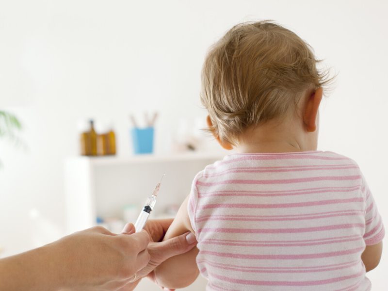 Bck View of baby girl patient receiving vaccine at the doctor's office, focus on hand holding vaccine